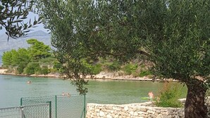 Un paisaje junto al lago con dos sillones blancos bajo un árbol, un muro de piedra y equipo para deportes acuáticos.