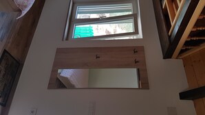 Una habitación con un espejo grande, dos ventanas y vigas de madera.