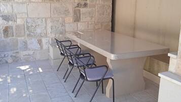 An outdoor seating area with a stone wall, a thatched roof, and a hanging light fixture.