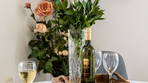 Ein Esstisch mit einer Weinflasche, zwei Gläsern, einem gewebten Korb und einer Vase mit rosa Rosen.