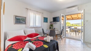 Ein Schlafzimmer mit einem Bett, roten Kissen, einer blumigen Tagesdecke, einem Fernseher und einem Balkon mit Tisch und Stühlen.