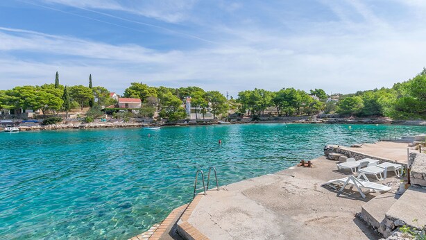 Ein klares, türkisfarbenes Schwimmbecken mit einer Betonplattform, Liegestühlen und einer Steintreppe, die ins Wasser führt.