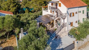 Ein zweistöckiges Haus mit Balkon, überdachter Terrasse und Blick auf die umliegende Grünfläche und Hügellandschaft.