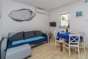 Huone, jossa on sohva, ruokapöytä tuoleineen, televisio ja ikkuna.