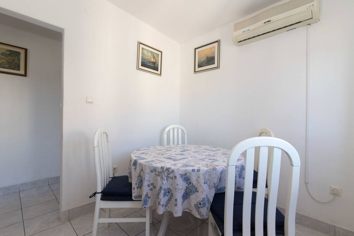 Un pequeño comedor con una mesa cubierta por un mantel estampado, dos sillas blancas y dos cuadros en la pared.