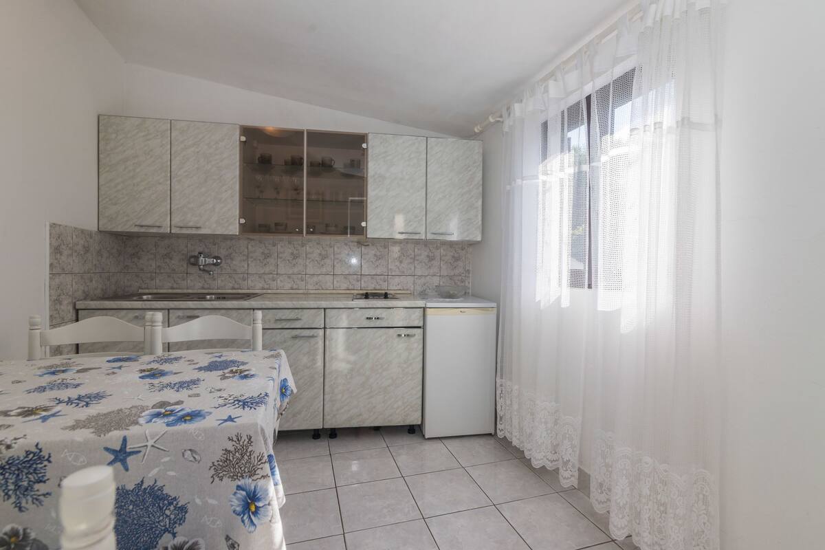 Una cocina compacta con armarios blancos, lavavajillas y un comedor con mesa para dos.