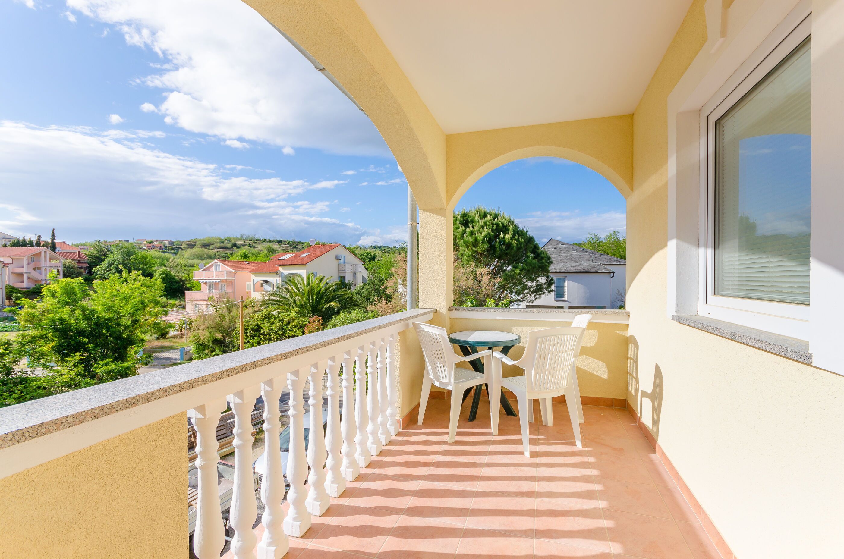 A balcony with a table and chairs, a view of the surrounding neighborhood, and a clear sky.