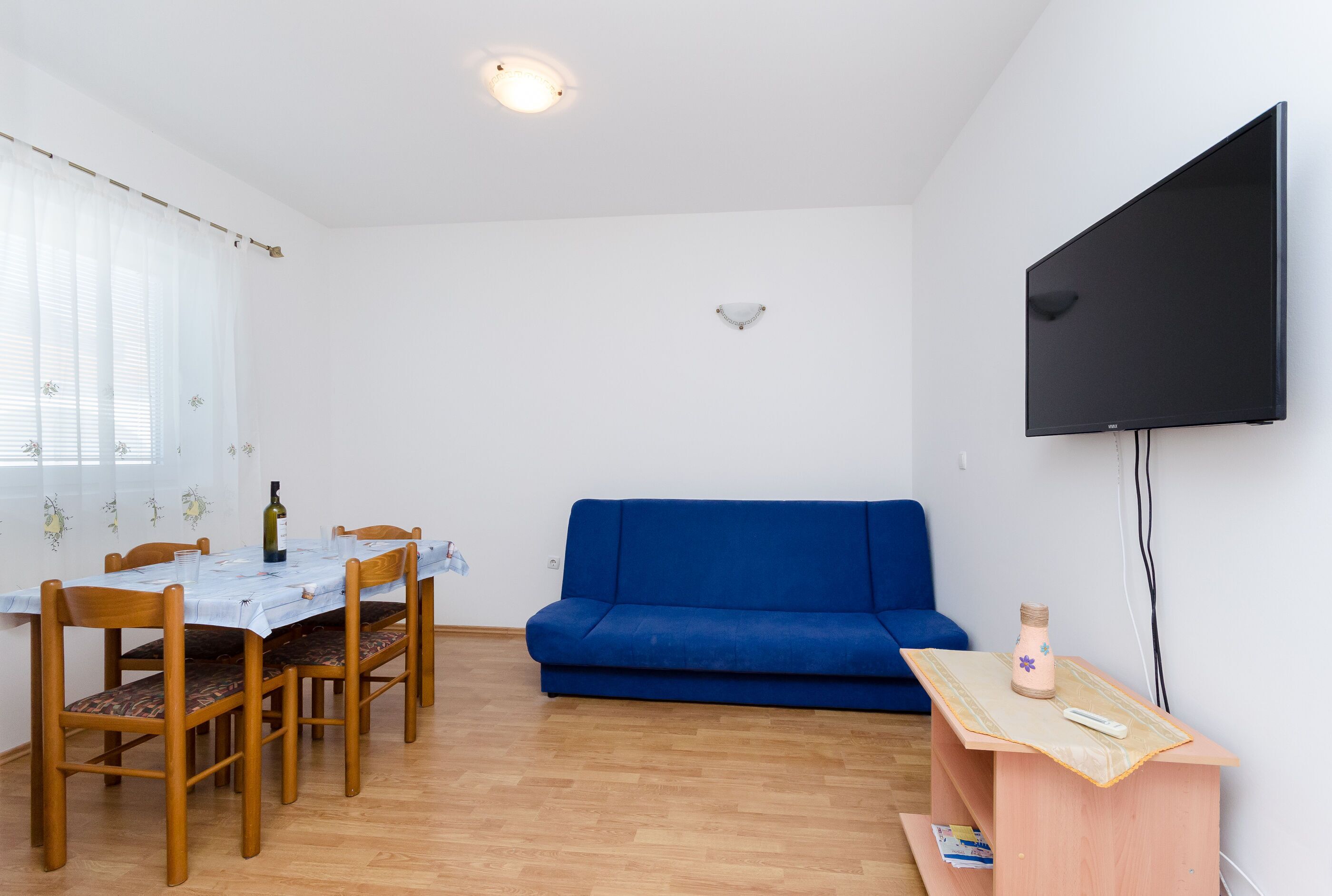 A room with a dining table, chairs, a blue sofa, a TV, and a wooden cabinet.