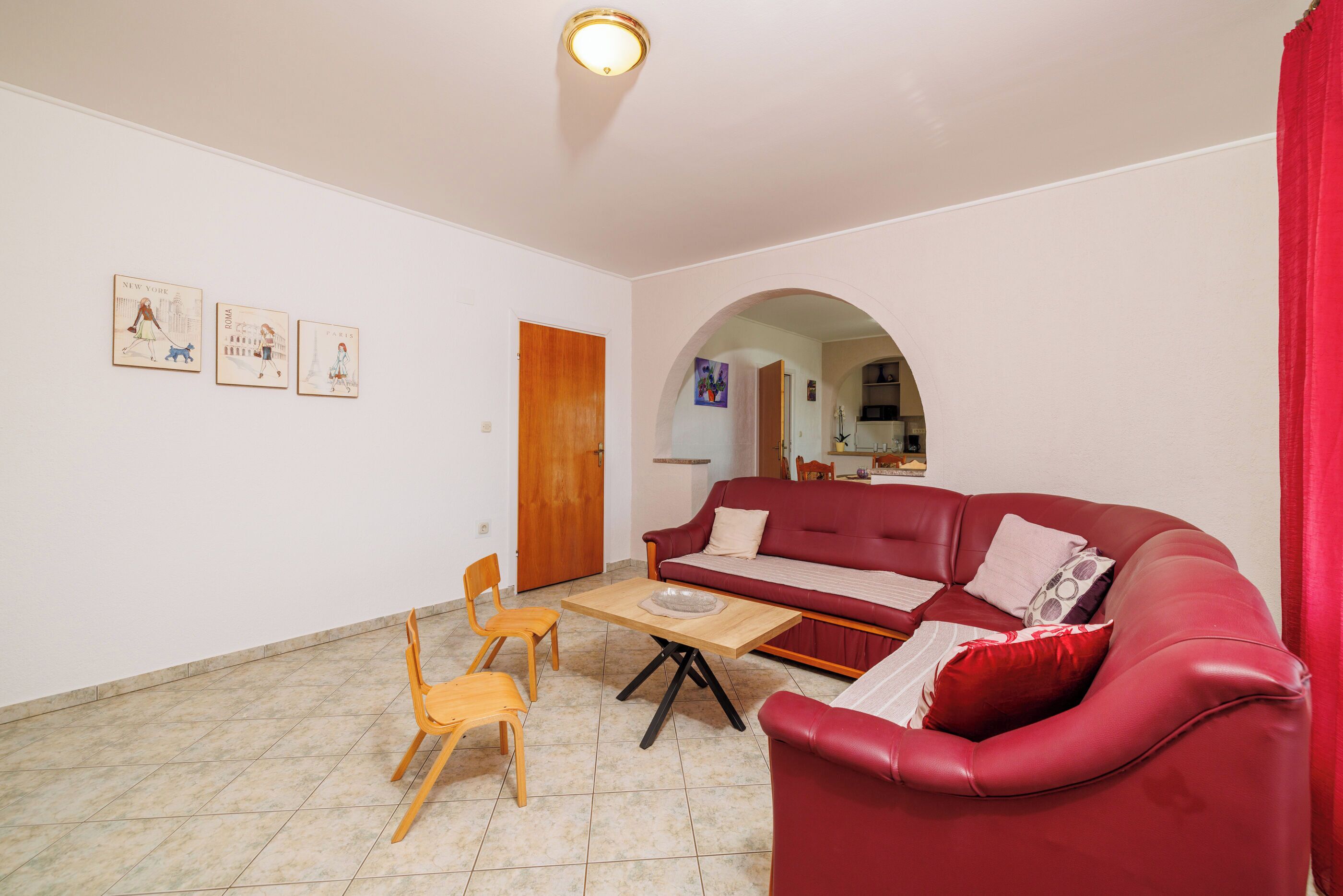 A living room with a red sofa, wooden chairs, a small table, and wall art depicting cities.