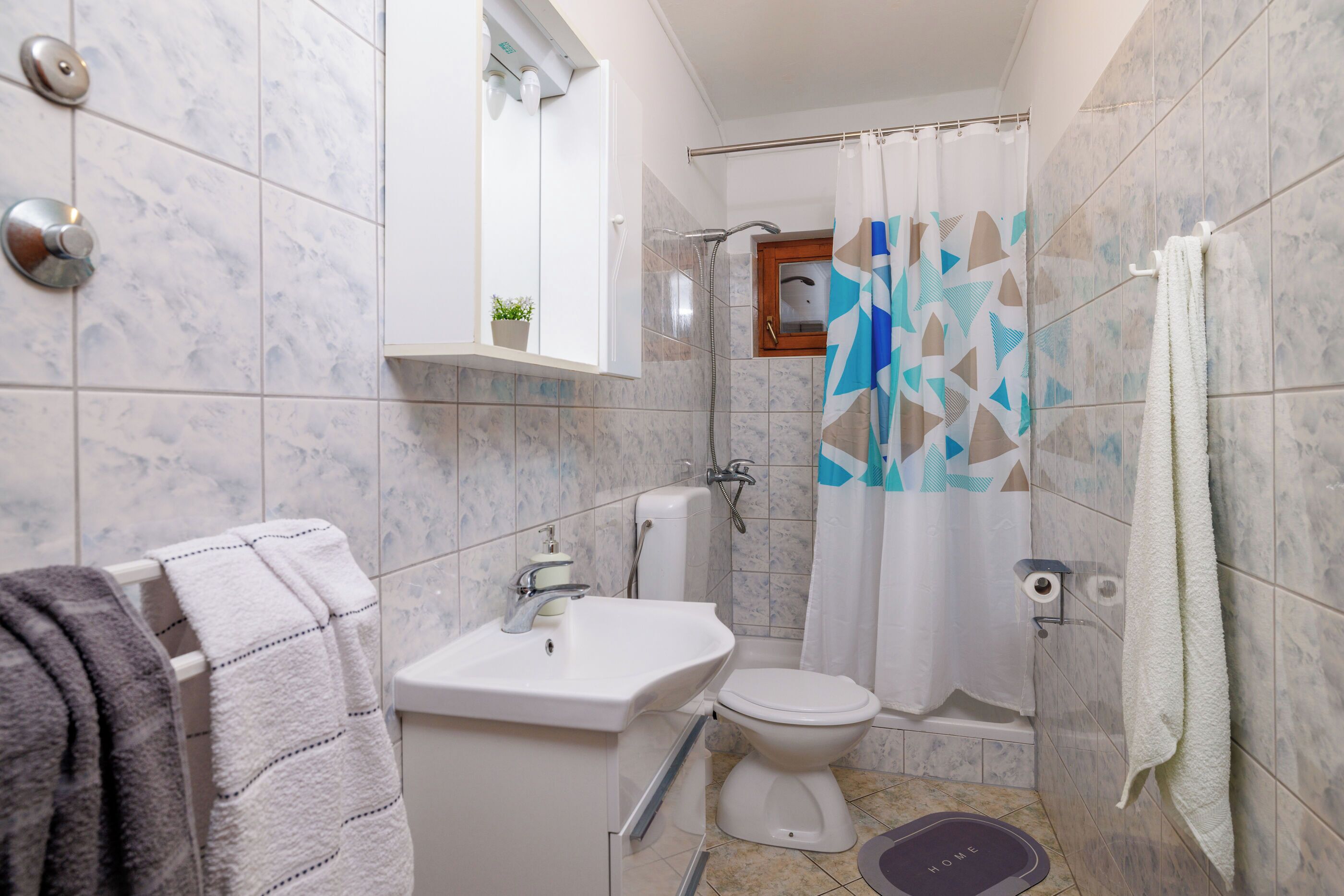 A bathroom with a toilet, sink, shower, and a towel rack.
