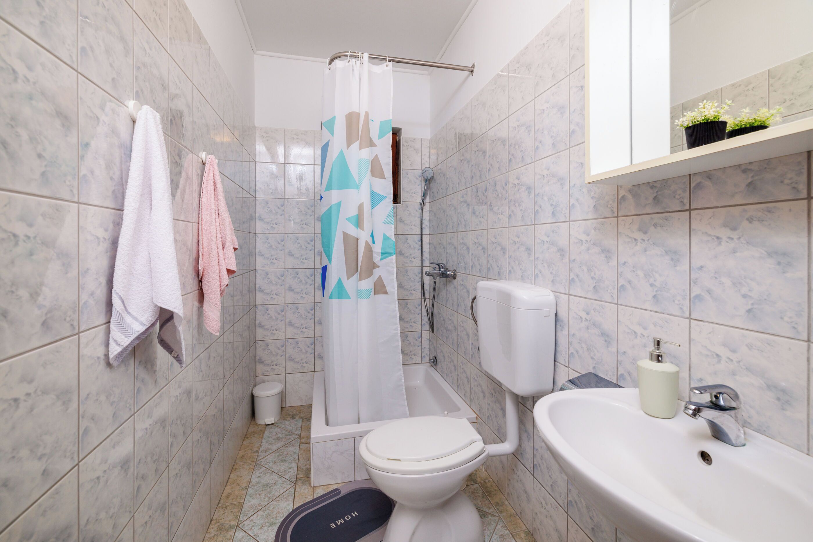 A bathroom with a toilet, sink, shower, and tiled walls.