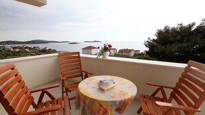 A balcony with wooden chairs and a table, overlooking a coastal view with houses and a body of water. - Apartments Lanterna (Rogoznica)