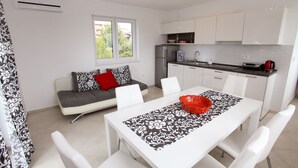 A compact living space with a dining area, kitchenette, and a sofa with patterned cushions. - Apartments Lanterna (Rogoznica)