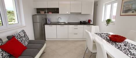 A compact kitchen with white cabinets, a stainless steel refrigerator, a sink, and a dining area with a white table and chairs.