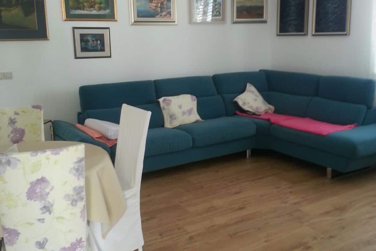 Un salon avec un canapé bleu, une petite table recouverte d’une nappe à motifs floraux et plusieurs tableaux encadrés accrochés au mur.