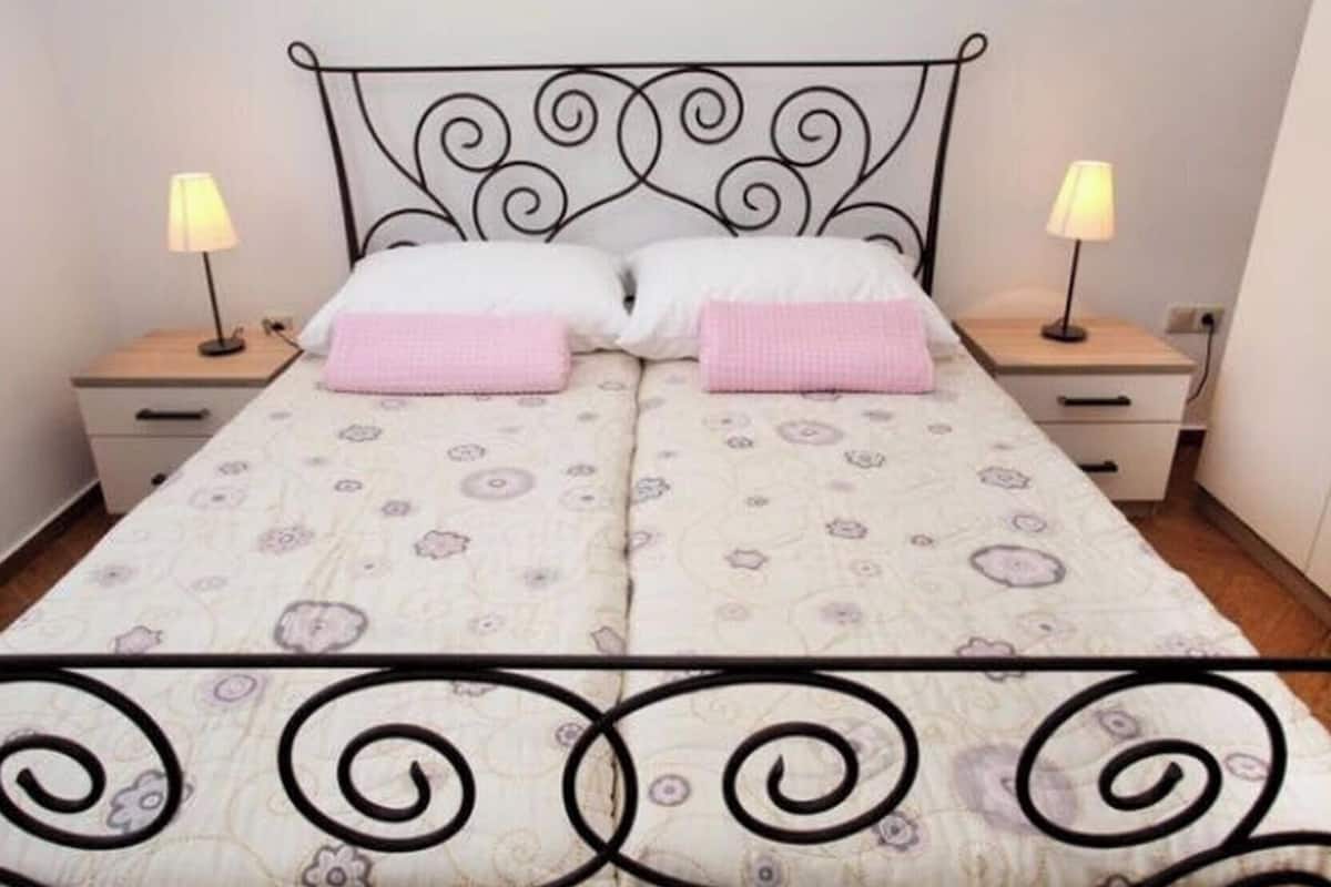 Un lit double avec une couvre-lit à motifs floraux, deux tables de chevet avec des lampes et une tête de lit décorative en métal.