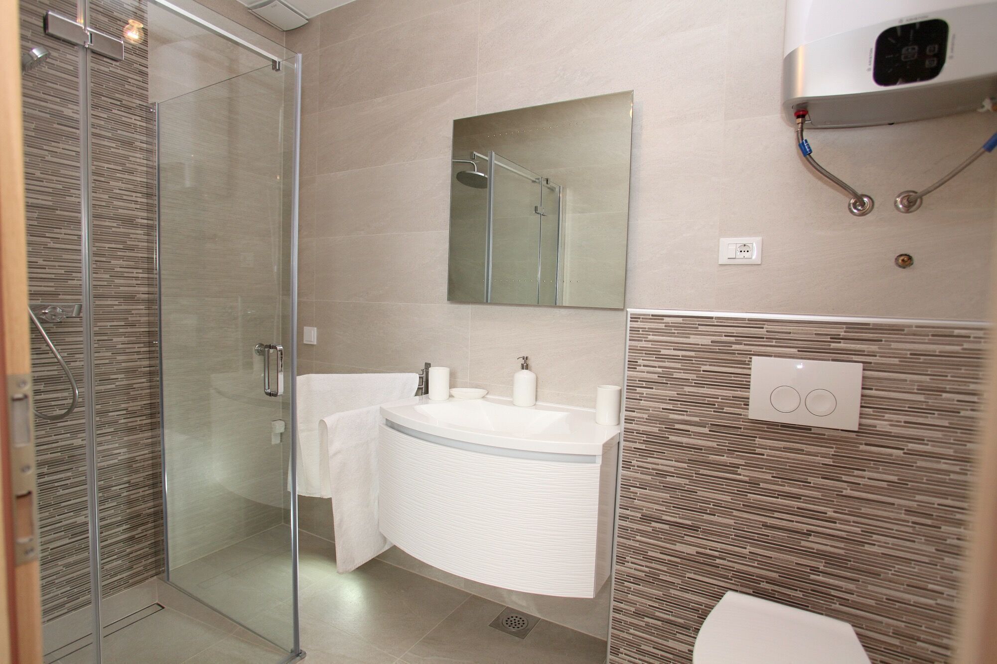 A modern bathroom with a glass shower enclosure, a white sink with a mirror above, and a toilet with a wall-mounted bidet.