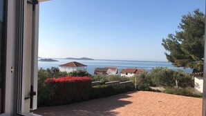 A view from a balcony with a paved area, a clear sky, and a distant body of water. - Apartments Lanterna (Rogoznica)