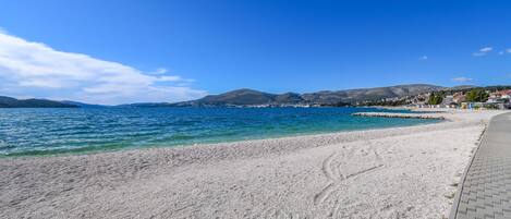 A pebble beach with a clear blue sea and distant mountains.