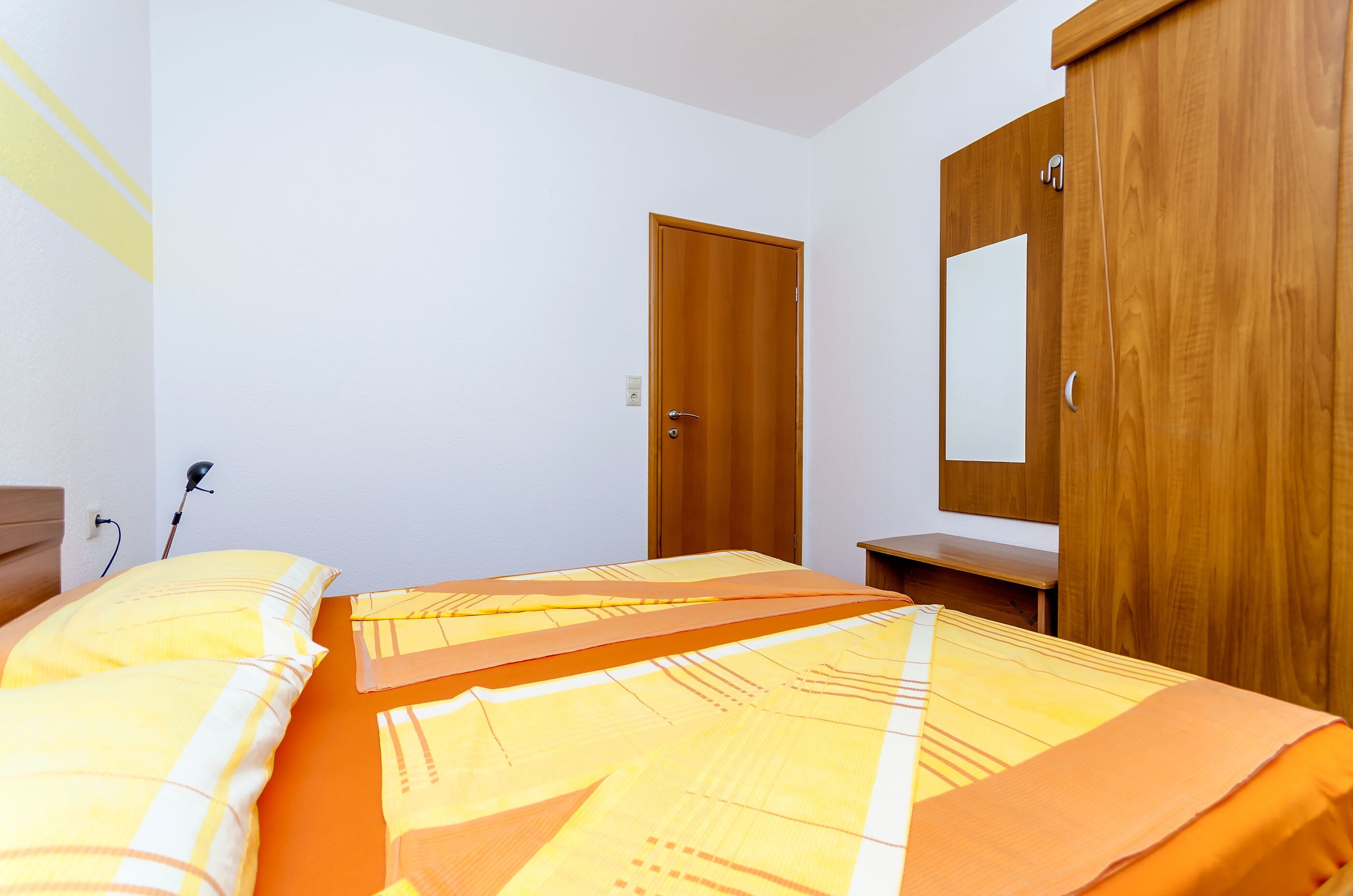 Een slaapkamer met een bed, een houten garderobe en een spiegel.