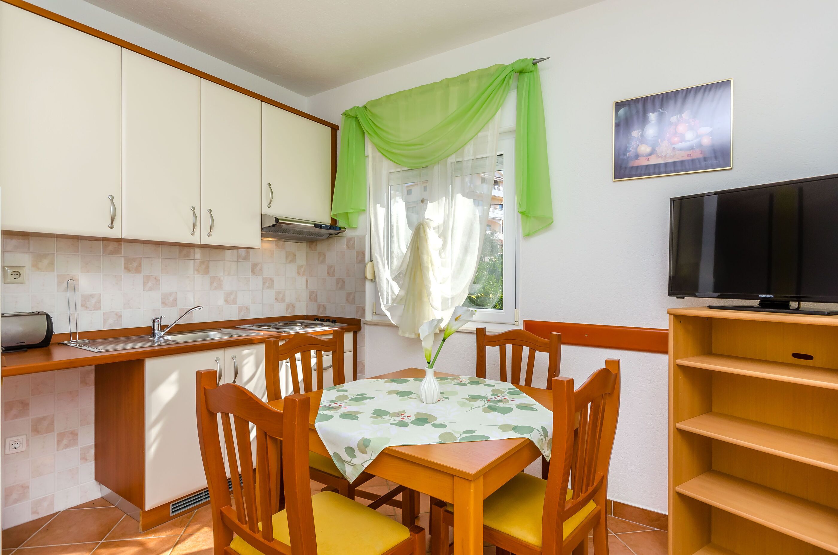 A compact kitchen with a dining area, a TV, and a window with green curtains.