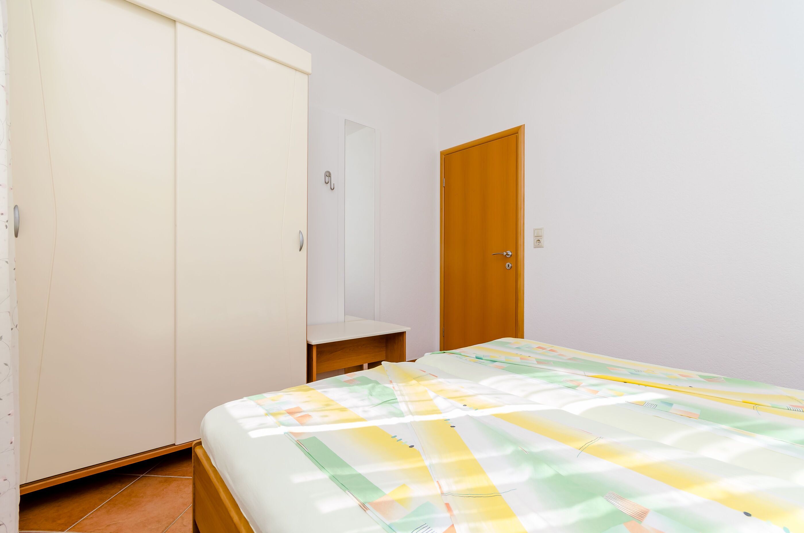 A bedroom with a bed, a wardrobe, a door, and a small shelf.