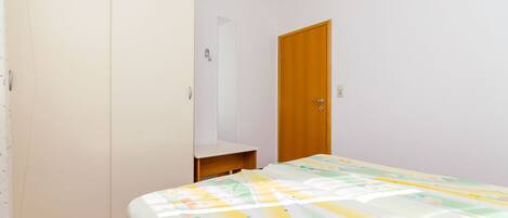 A bedroom with a bed, a wardrobe, a door, and a small shelf.