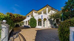 Un immeuble de deux étages avec une allée pavée, une entrée fermée par un portail et un balcon.