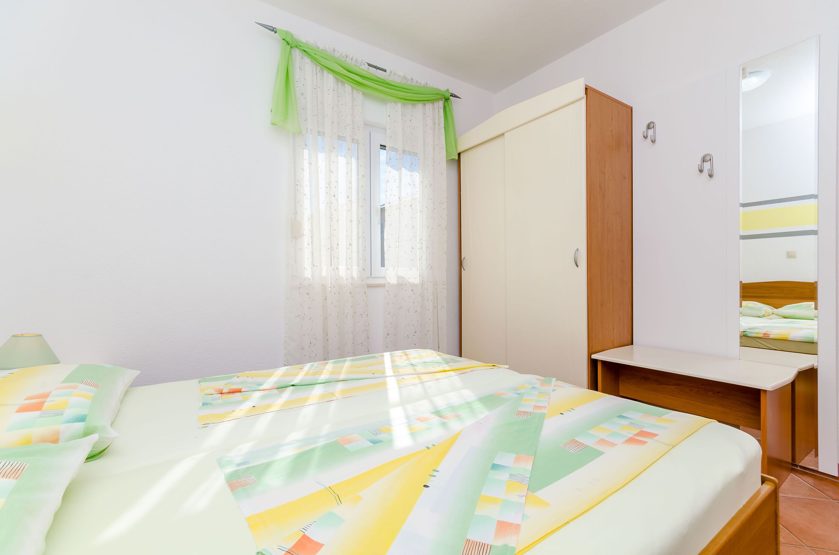 A bedroom with a bed, a desk, a wardrobe, and a mirror.