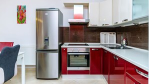 Une cuisine moderne dotée d’un réfrigérateur en acier inoxydable, d’un four encastré et de meubles de rangement rouges.