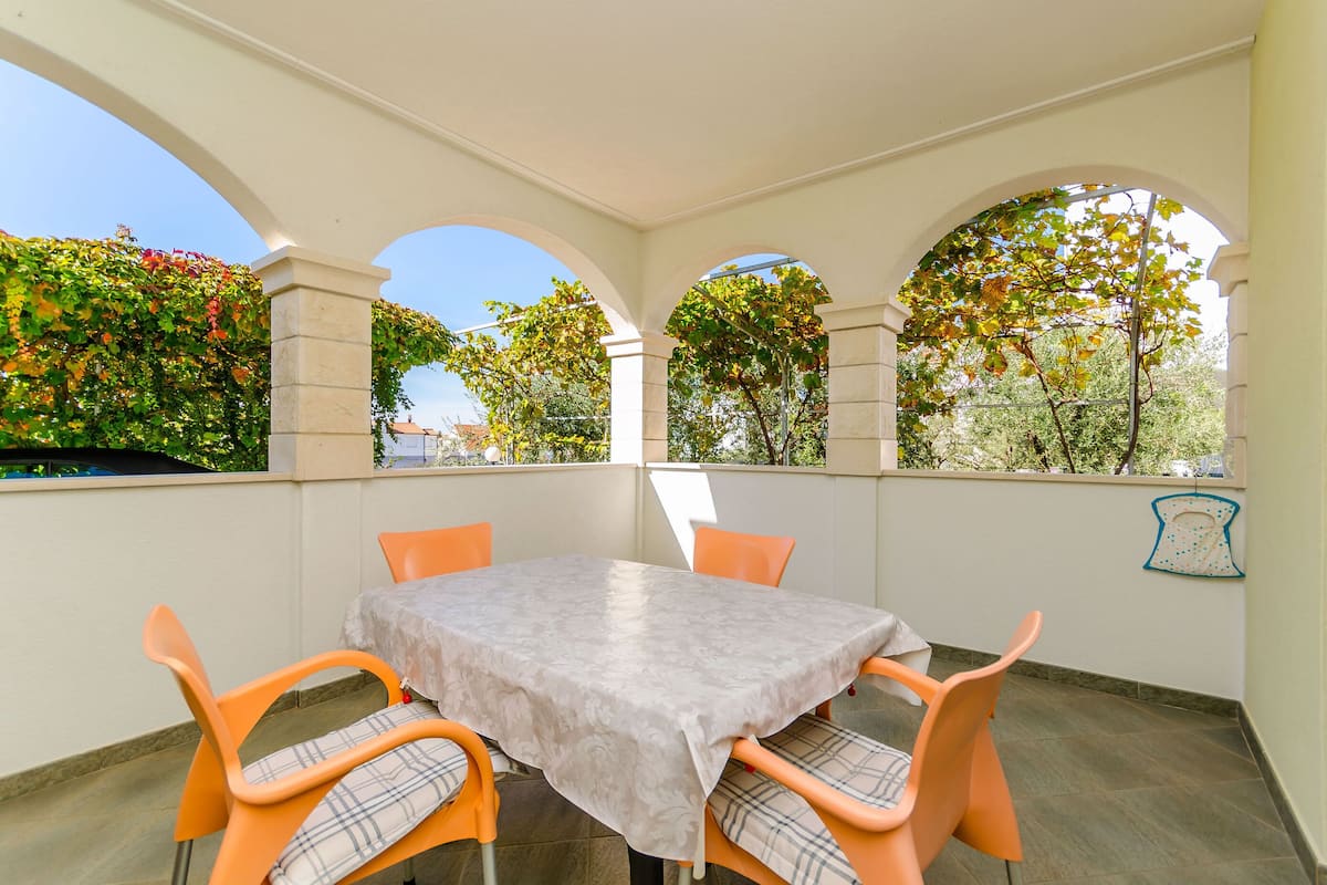 A covered patio with a table and chairs, surrounded by arches and greenery.