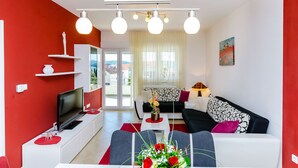 Un salon moderne avec un mur d’accent rouge, un téléviseur à écran plat, un canapé et une table basse agrémentée d’un arrangement floral.