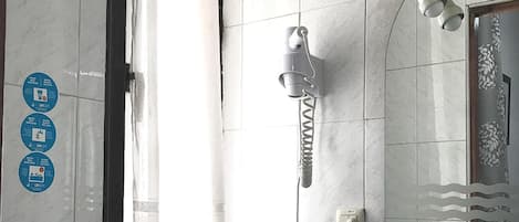 Un baño con ducha, lavabo, inodoro y espejo. Hay letreros en la pared y una cortina que cubre parcialmente la ventana.