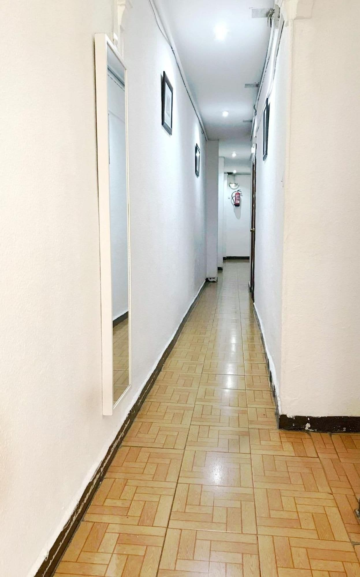 Un pasillo con piso de espiga, paredes blancas y un extintor de incendios montado en la pared.