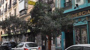 A street with parked cars and buildings with balconies and storefronts.