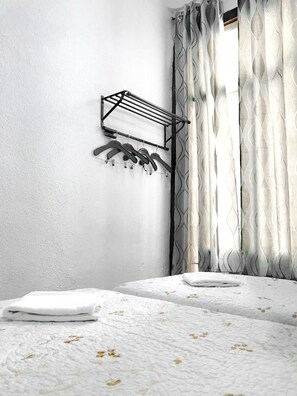 A bedroom with a bed, a wall-mounted drying rack, and a window with patterned curtains. - Hostal Los Arcos (Madrid)