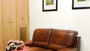 Un sofá de cuero marrón, una mesa blanca con un florero y dos cuadros en la pared.