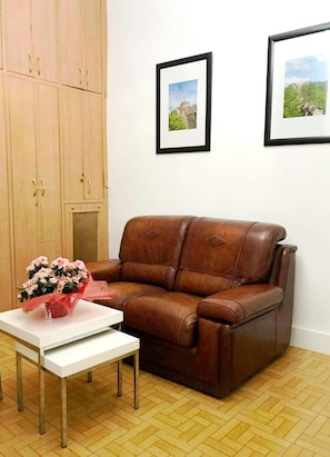 Un sofá de cuero marrón, una mesa blanca con un florero y dos cuadros en la pared.