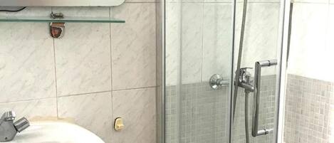A bathroom with a glass-enclosed shower, a white sink, and a mirror with a decorative frame.