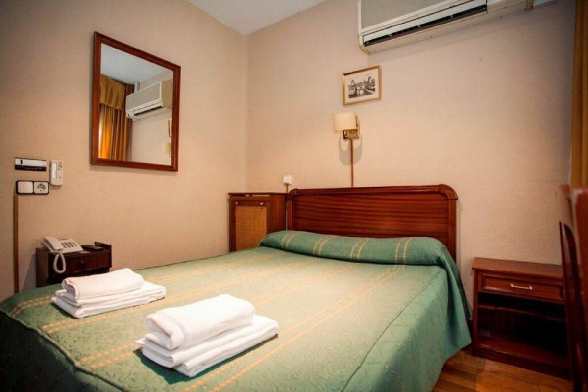 A hotel room with a bed, a bedside table, a lamp, and a mirror.