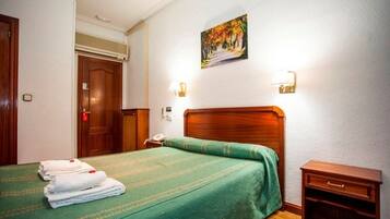 A hotel room with a wooden bed, green bedspread, two bedside lamps, a painting on the wall, and a wooden nightstand.