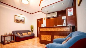 A reception area with a wooden reception desk, a grey sofa, a red sofa, and a blue chair. - Pensión Carrera (Madrid)