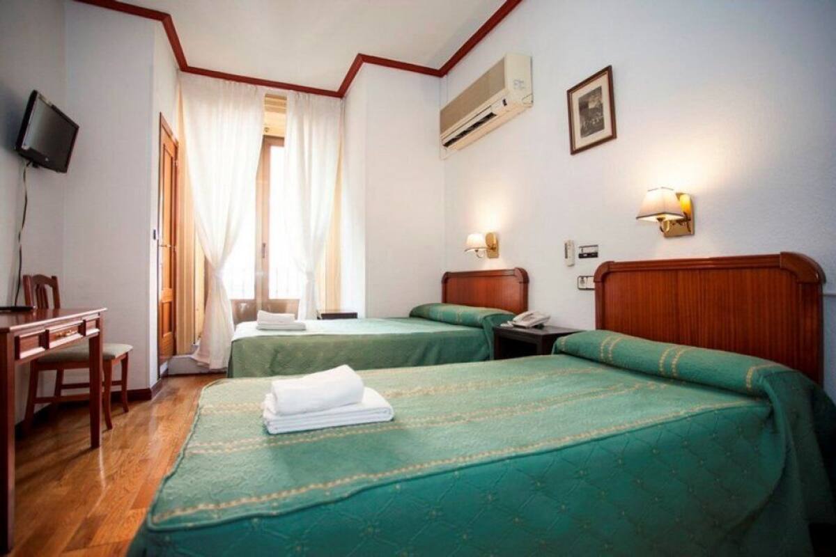 A hotel room with two beds, a desk, a chair, a television, and a window with curtains.