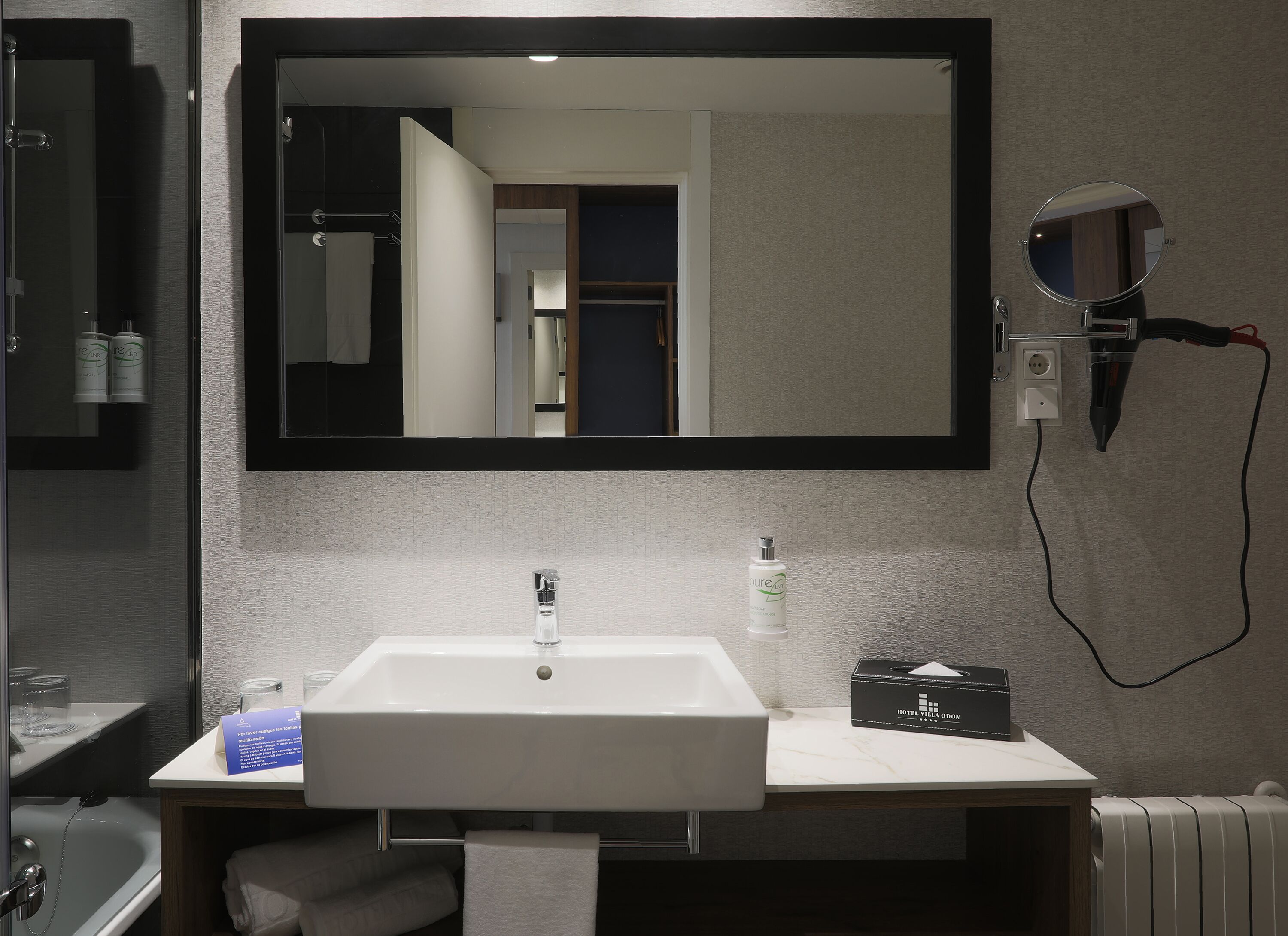 A modern bathroom with a large mirror, a sink, a towel rack, and a hairdryer on a wall-mounted charging station.