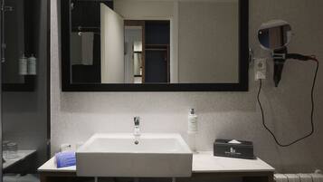 A modern bathroom with a large mirror, a sink, a towel rack, and a hairdryer on a wall-mounted charging station.