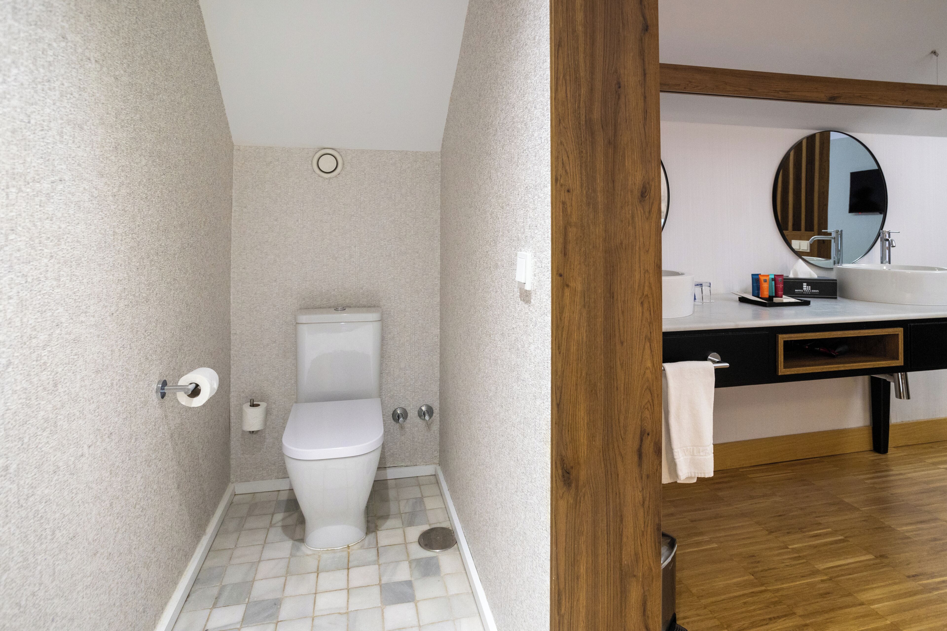 Een badkamer met toilet, wastafel, spiegel en houten vloer.