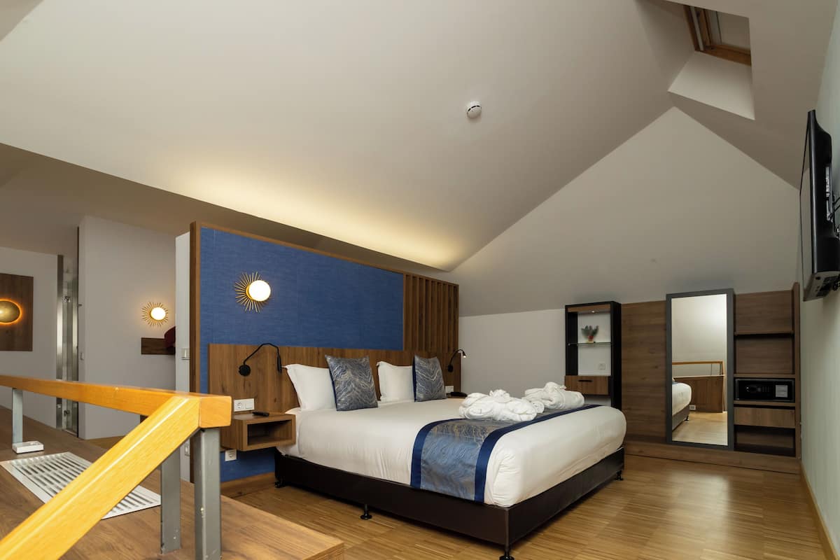A modern bedroom with a bed, wooden headboard, bedside tables, a mirror, and a staircase.