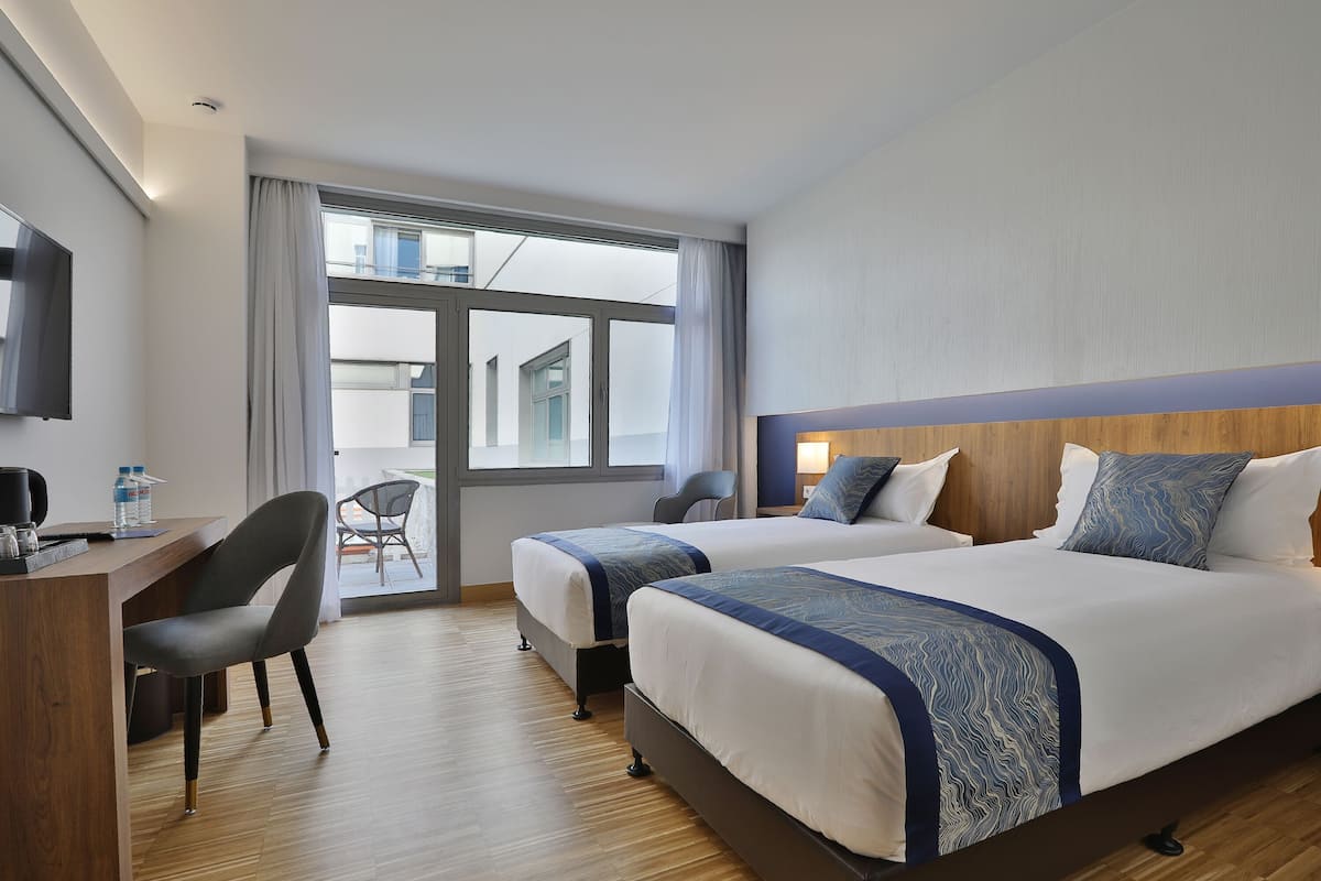 A hotel room with two beds, a desk, a chair, and a TV.