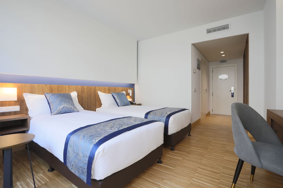 A hotel room with two beds, a desk, and a chair.