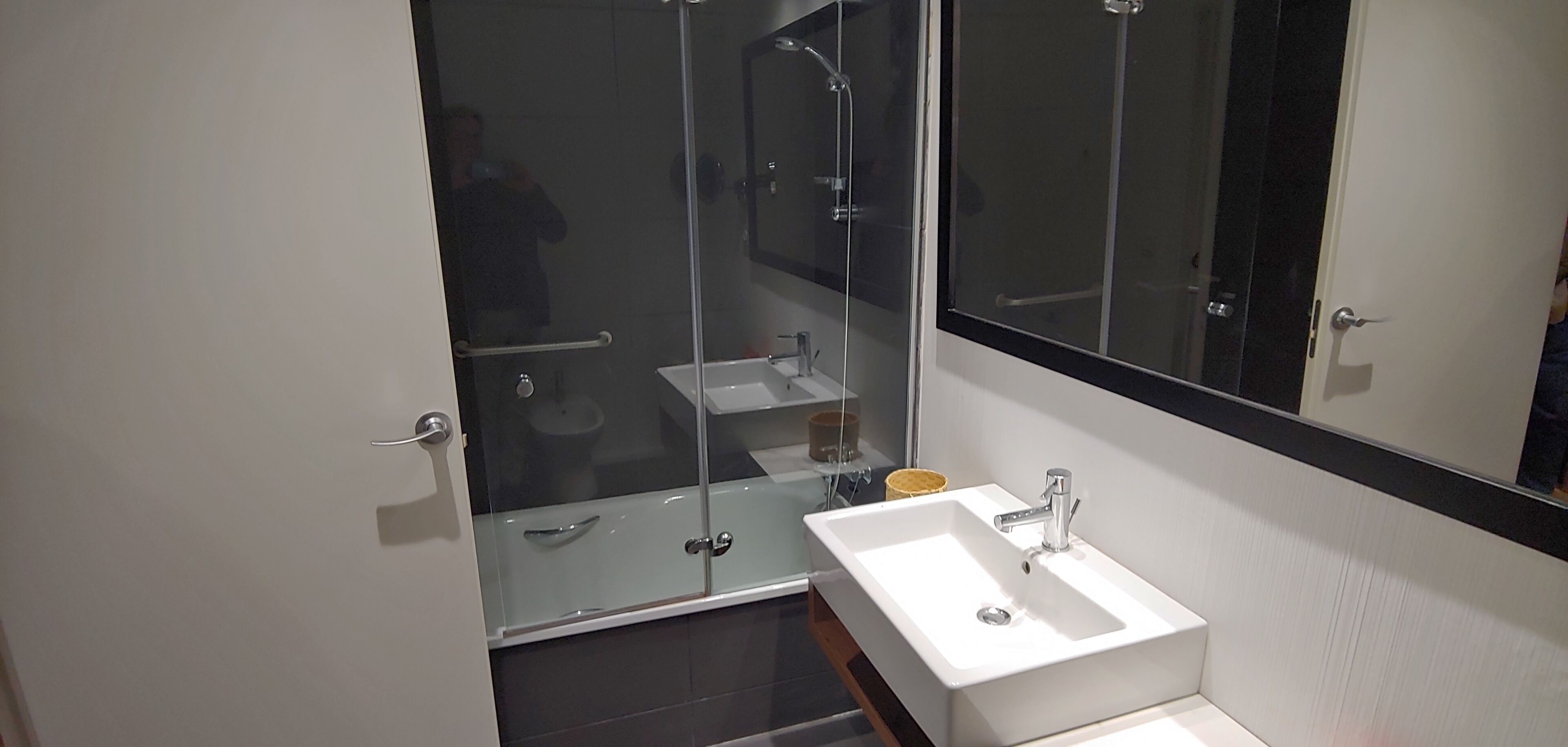 Une salle de bain moderne avec une douche à l’italienne en verre, un lavabo blanc et un grand miroir.